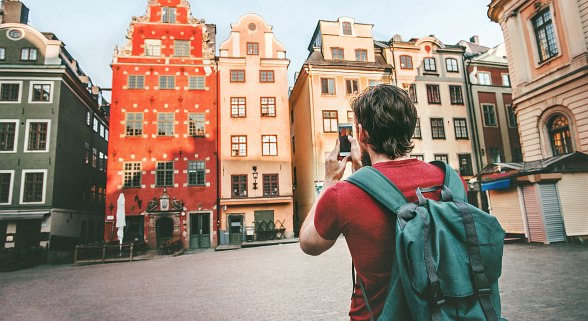 Junger Mann steht im Rundreise Urlaub vor einem Antiken Gebäude und macht ein Foto auf seinem Smartphone