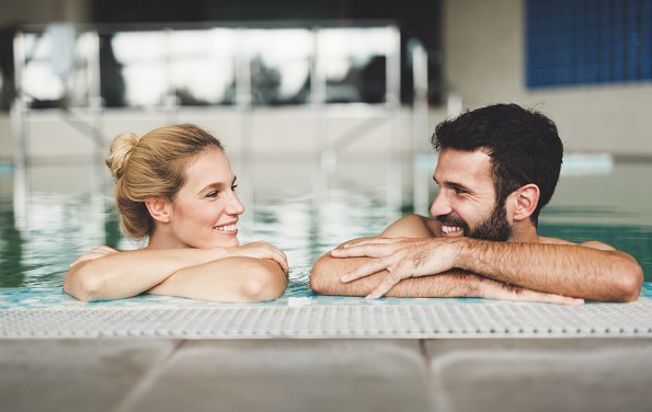 Frau und Mann im Innenpool eines Hotels schauen sich lächelnd an