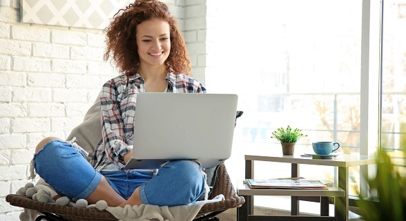 Junge Frau sitzt lächelnd vor dem Laptop
