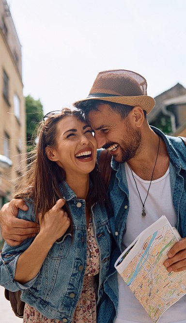 Junges Paar mit Hut und Stadtplan erkundet lachend eine europäische Stadt