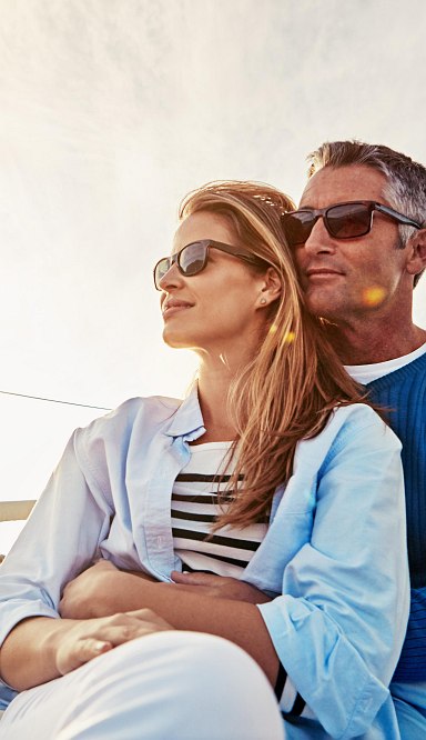 Frau und Mann sitzen auf einem Schiff und haben haben den Sonnenuntergang im Hintergrund