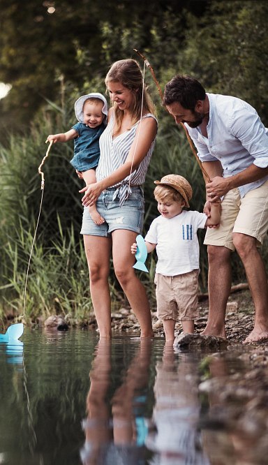 Familie mit zwei Kindern stehen am Ufer eines Sees.