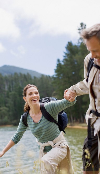 Mann gibt Frau die Hand beim Wandern, im Hintergrund ein See