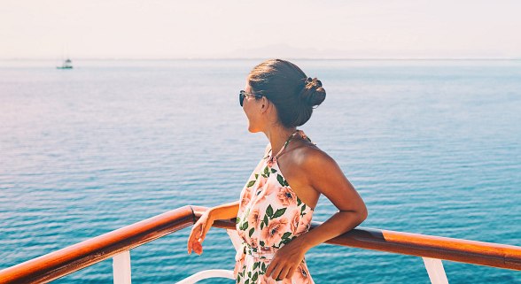 Frau steht auf Deck bei einer Kreuzfahrt und sieht auf das Meer