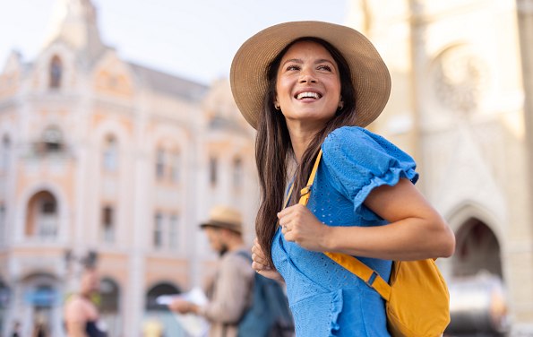 Junge Frau mit Hut, blauem Kleid und Rucksack auf Städtetour