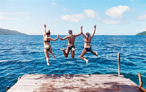 Drei junge Frauen hüpfen von Steg in den See 