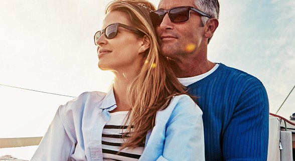 Frau und Mann sitzen auf einem Schiff und haben den Sonnenuntergang im Hintergrund