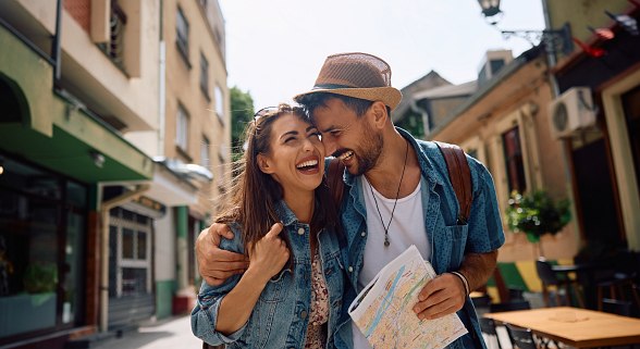 Junges Paar lachend mit Hut und Stadtplan in der Hand erkunden eine europäische Stadt