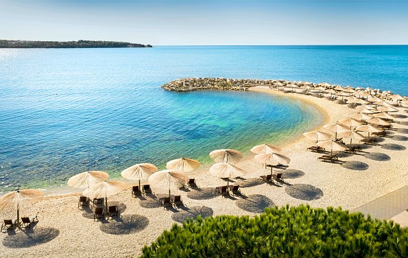 Türkisblaues Meer mit Strandbucht und Sonnenliegen