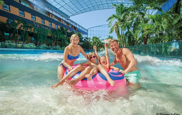 Familie mit zwei Kindern auf einem großen Schwimmreifen im Wasser. Im Hintergrund Palmen in der Therme Erding 