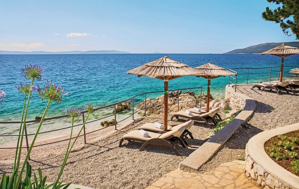 Zwei Strandliegen mit Sonnenschirm direkt am Strand und blauem Meer im Hintergrund