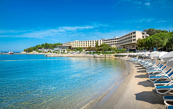 Blaues Meer mit Sandstrand und Liegestühlen. Hotel im Hintergrund