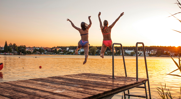 Zwei Frauen haben Spaß im gemeinsamen Urlaub und springen vom Steg in das Wasser